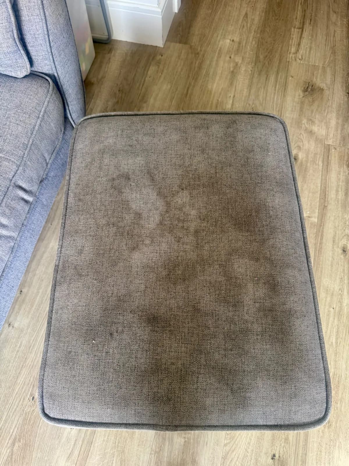 A marked grey upholstery cushion before professional cleaning